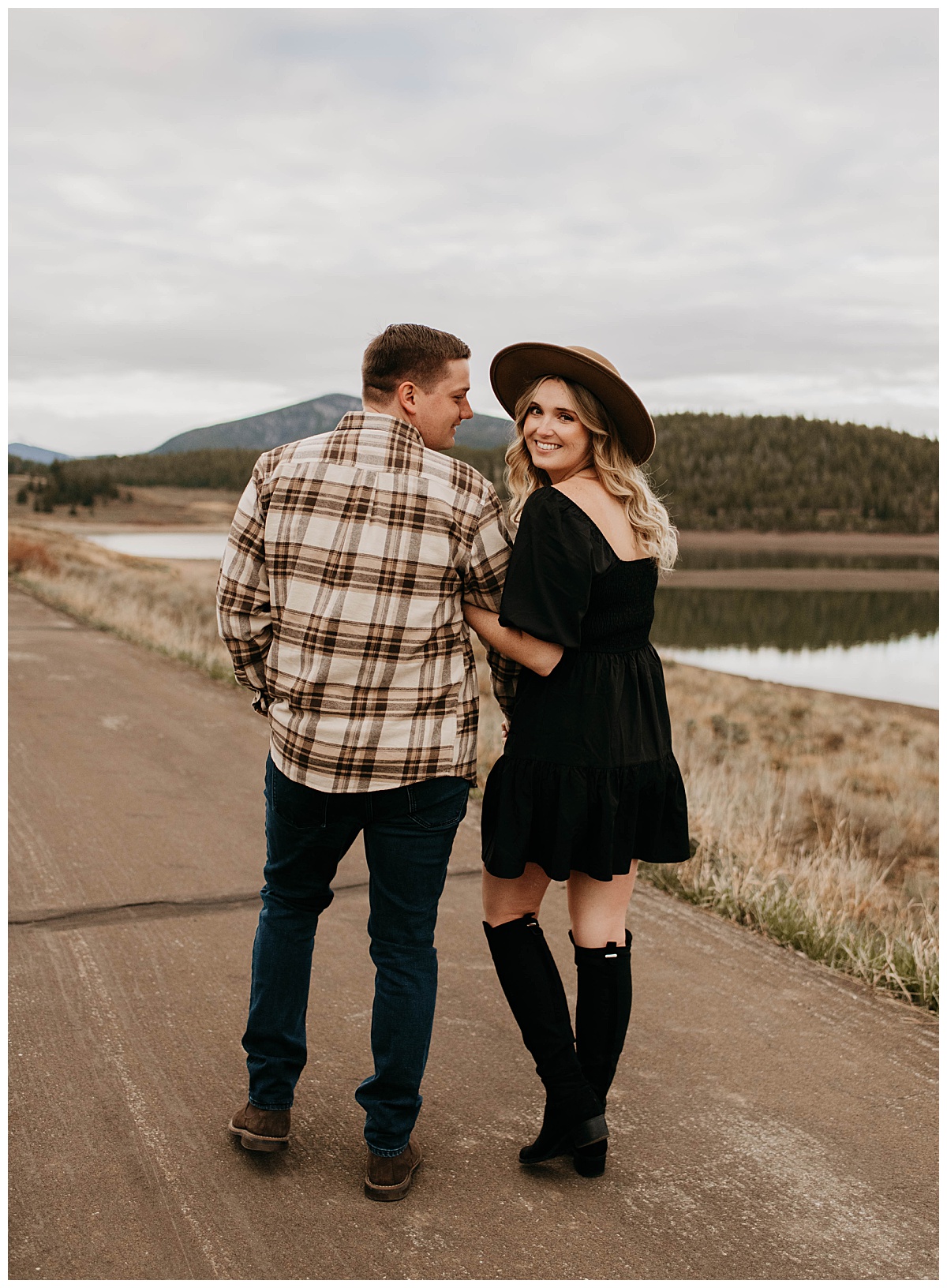 couple walks down road together while woman looks back smiling at Colorado engagement session