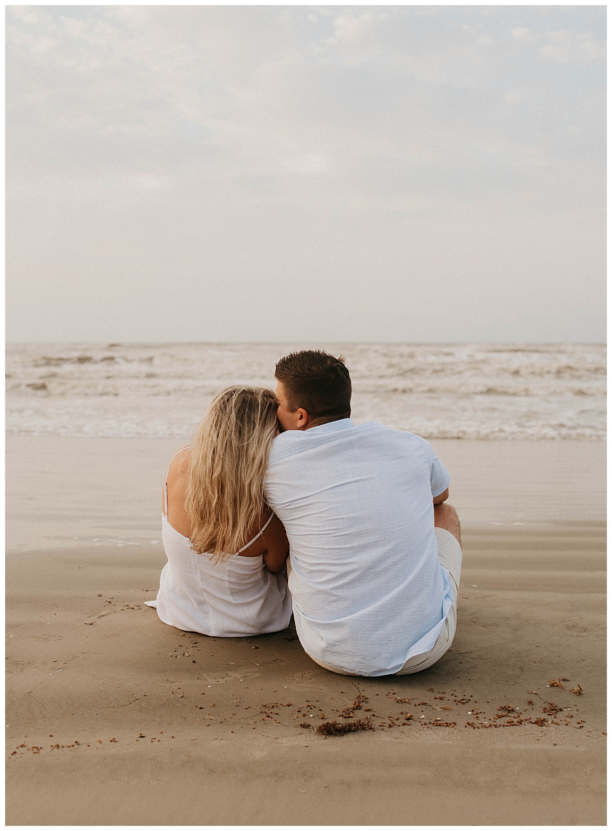 couple sits on sand facing water as they lean together by Stephanie J. Zamora Photography