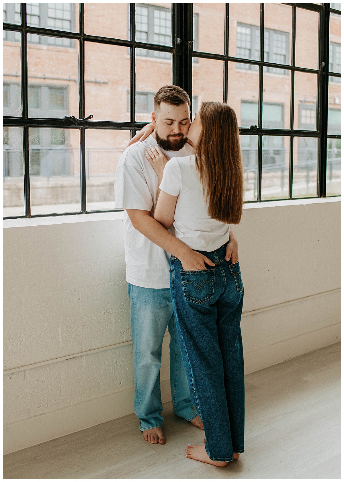 man leans against wall as woman kisses his cheek at studio engagement session