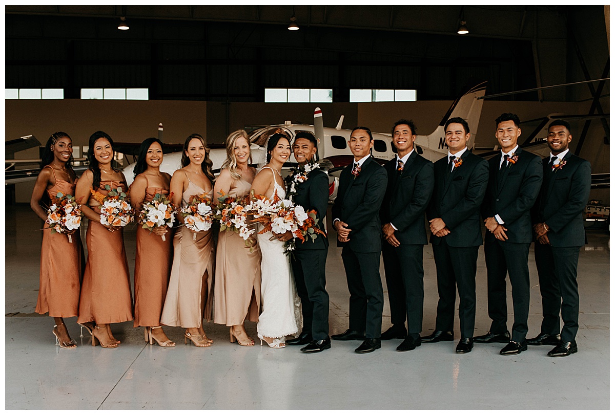 wedding party stands together in airplane hangar by Stephanie J Zamora Photography