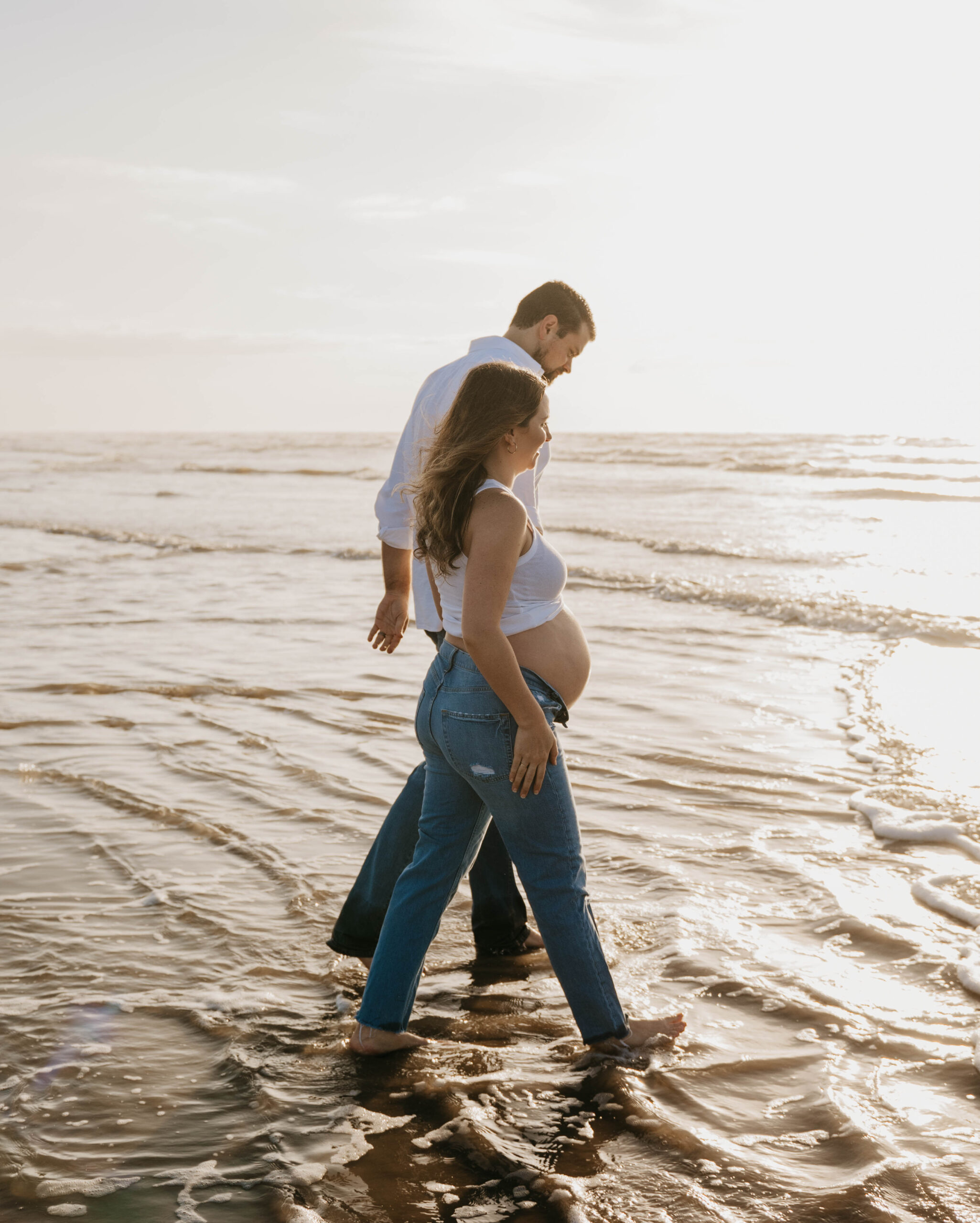 man and woman walk through ocean water at sunrise houston family and maternity photographer